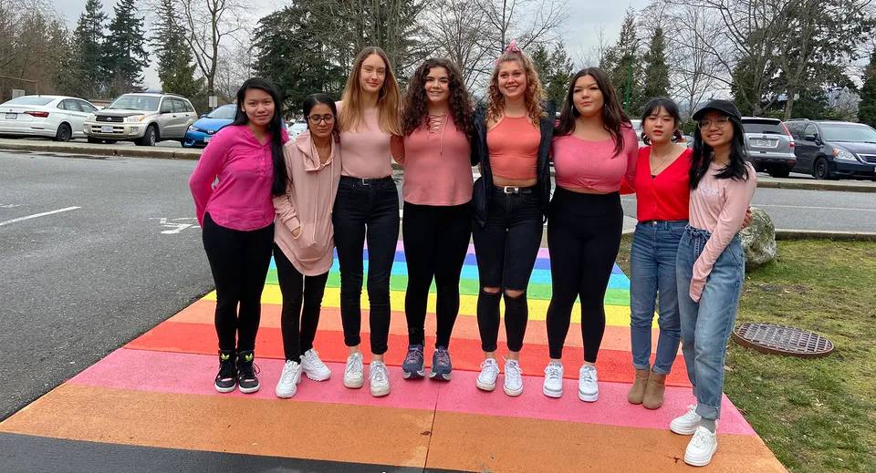 Un gruppo di studentesse della Cariboo Hill School si trova su una terrazza esterna colorata davanti ad alberi e veicoli parcheggiati.