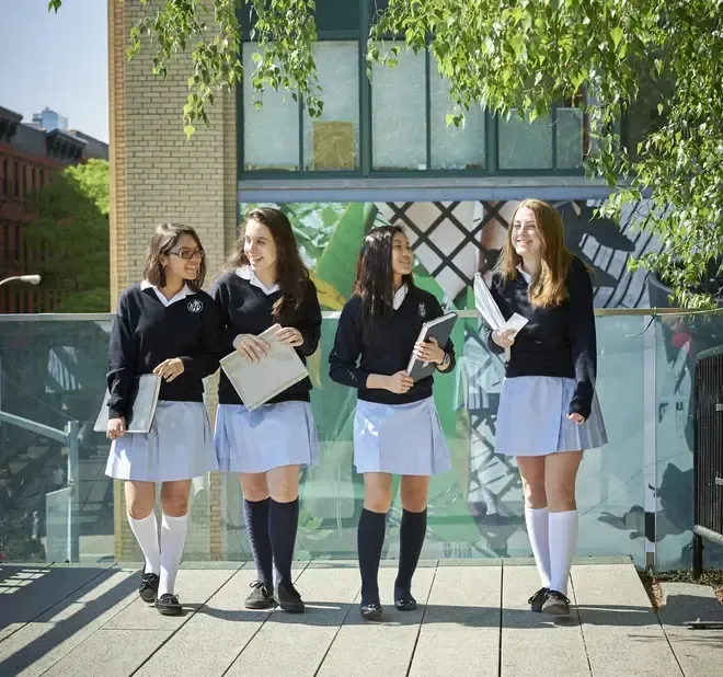 Un grupo de alumnas de Notre Dame High School está de pie frente a un edificio de ladrillo con grandes ventanas.