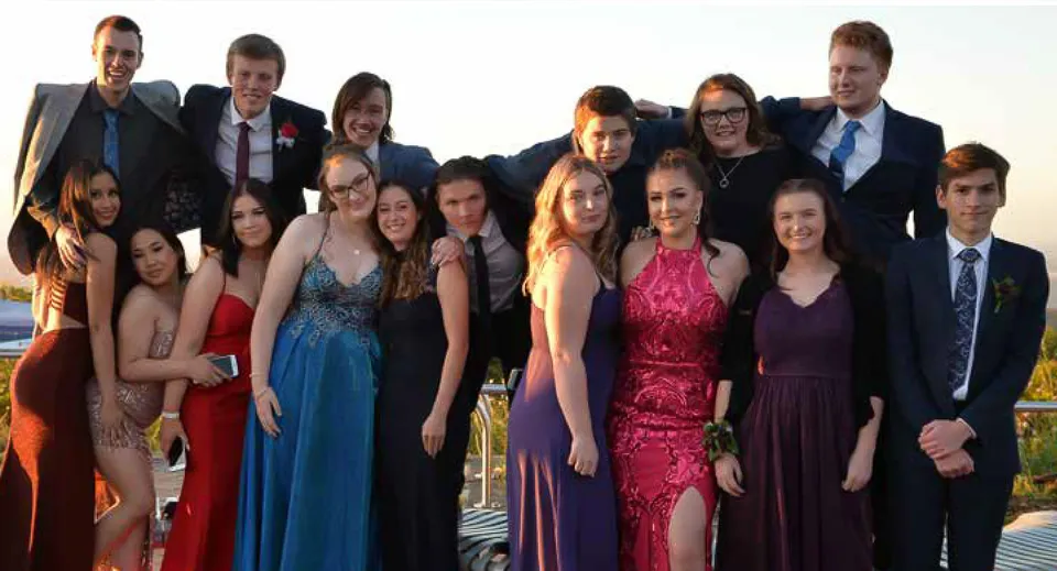 Un gruppo di persone ben vestite si trova insieme davanti a uno sfondo paesaggistico sul terreno della Oakbank Area School.