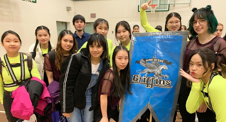 Un gruppo di studentesse della R.C. Palmer Secondary School posa con un grande striscione blu recante il logo della squadra sportiva.
