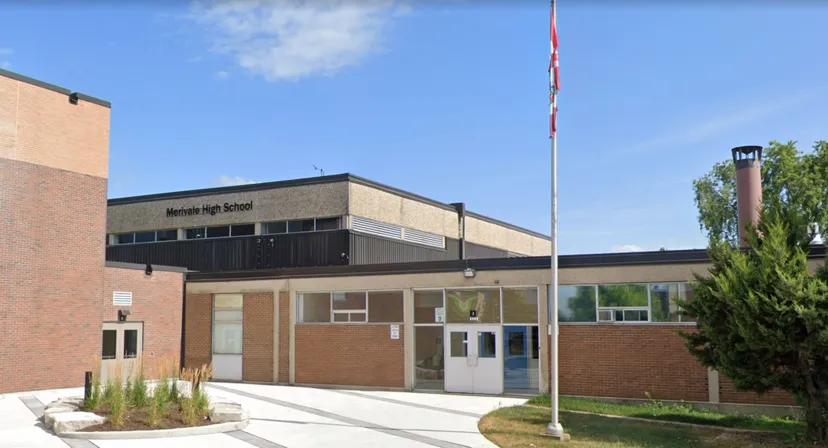 L'edificio in mattoni della Merivale High School è circondato da un'area pavimentata e piantumazioni, visibile sotto un cielo blu.