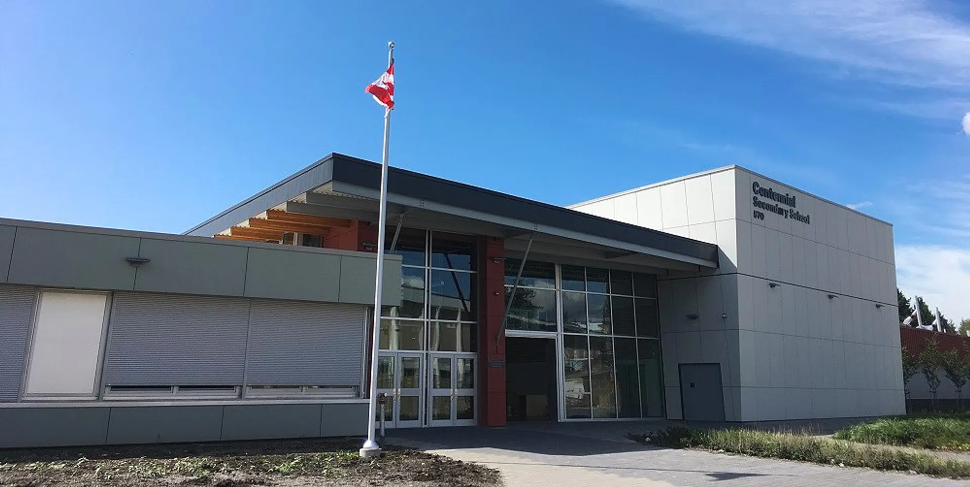 L'edificio moderno della Centennial Secondary School in British Columbia con una bandiera canadese sotto un cielo azzurro e limpido.