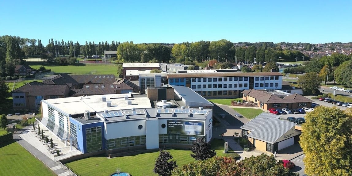 Luftbild des St John Plessington Catholic College mit Schulgebäuden, Sportplätzen und Bäumen