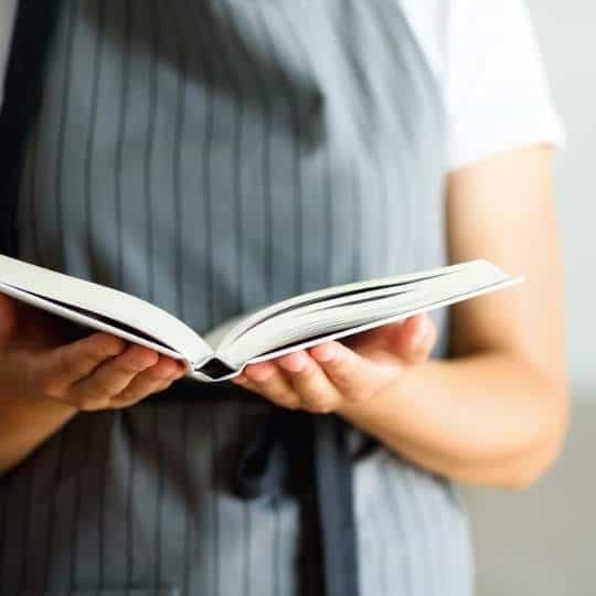 Persona con delantal gris a rayas sosteniendo un libro abierto en sus manos