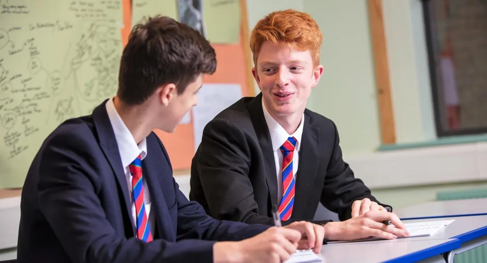 Due studenti della Loughborough Grammar School chiacchierano a un banco in classe davanti a una lavagna.
