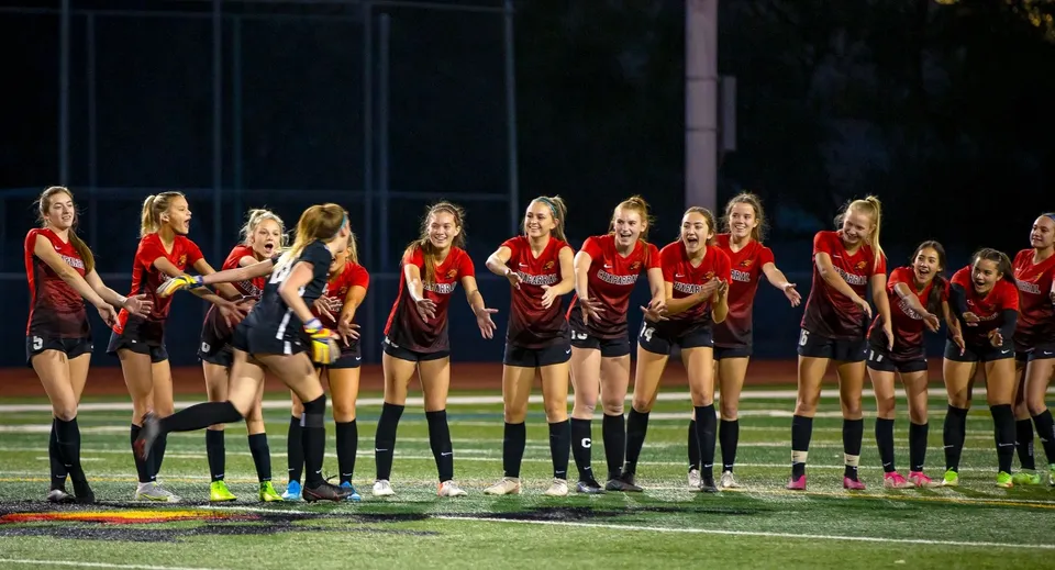 Un gruppo di giovani atlete della Quad Cities Christian School in maglia rossa su un campo sportivo di notte.