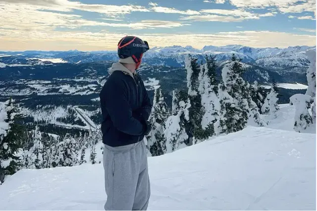 Ragazzo con casco da sci osserva il panorama innevato dalla cima di una montagna