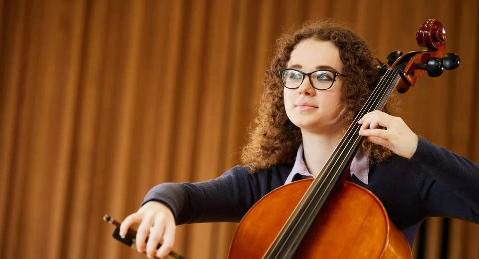 Una studentessa delle Haberdashers' Monmouth Schools suona il violoncello su un palco con un sipario sullo sfondo.