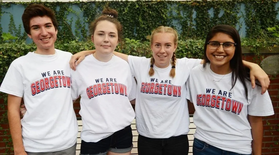 Quattro studenti della Georgetown District High School sono insieme davanti a uno sfondo di siepi verdi e indossano t-shirt bianche con la scritta We are Georgetown.