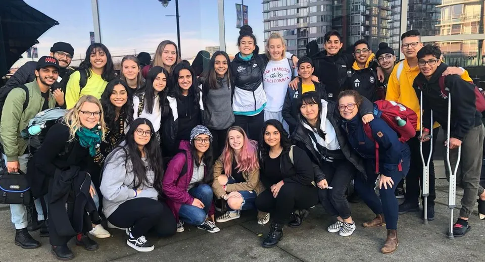 Un gruppo di studentesse si trova davanti ad alti edifici e sotto un cielo nuvoloso nel campus della Abbotsford Senior Secondary School.