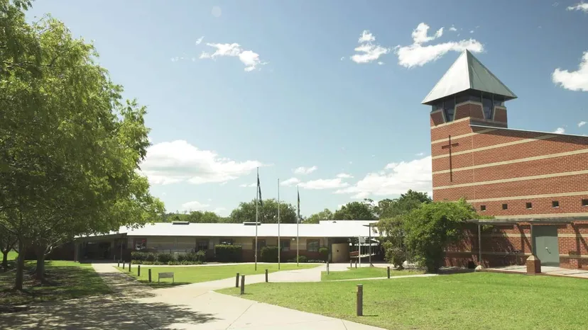 Il campus della Macarthur Anglican School con edifici in mattoni, una torre con una croce e prati verdi.