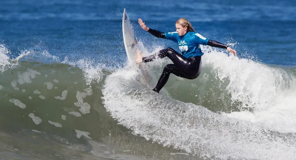 Un surfista cavalca una grande onda nell'oceano con il cielo limpido sullo sfondo, foto scattata presso il Whites Hill State College.
