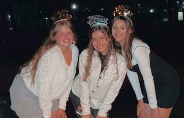Tres jóvenes sonrientes posan de noche al aire libre con diademas festivas de Año Nuevo