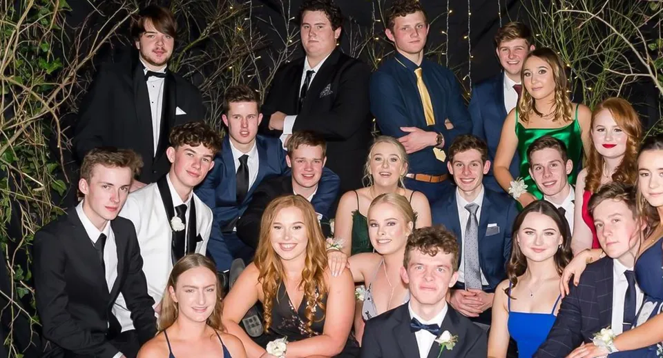 Un gruppo di studentesse e studenti del Kuranui College in abbigliamento formale posa all'aperto davanti agli alberi.