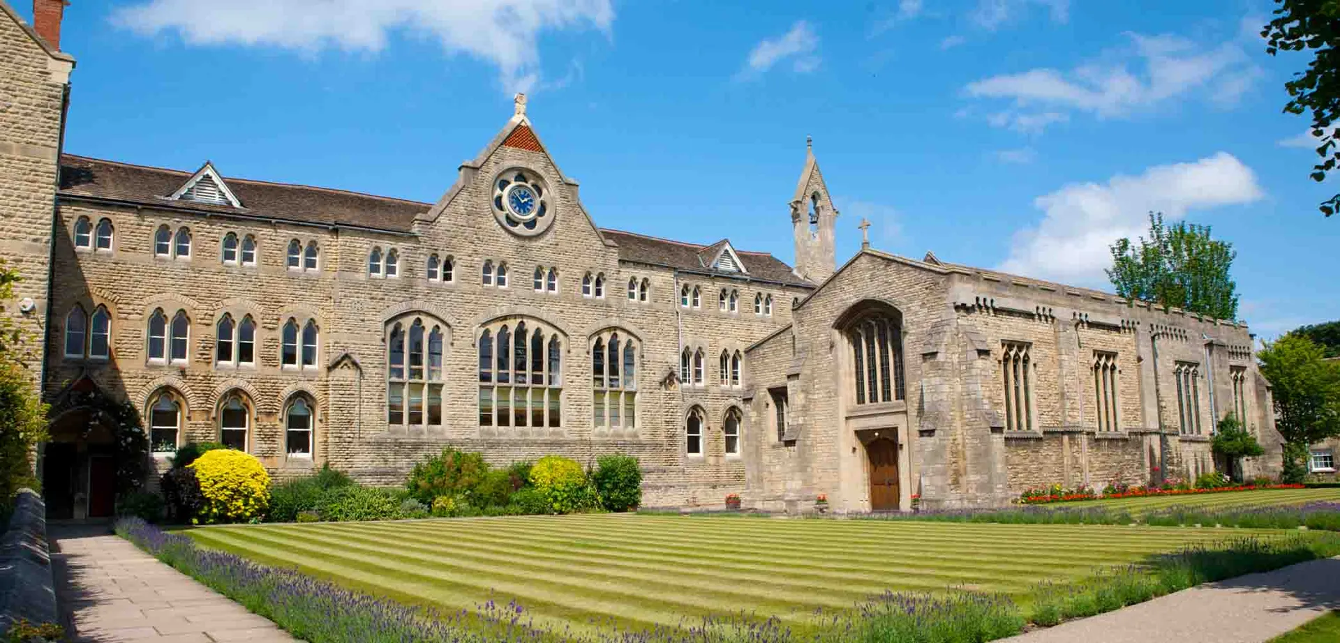 L'edificio principale storico della Stamford Endowed Schools con una torre dell'orologio e un giardino ben curato in primo piano.