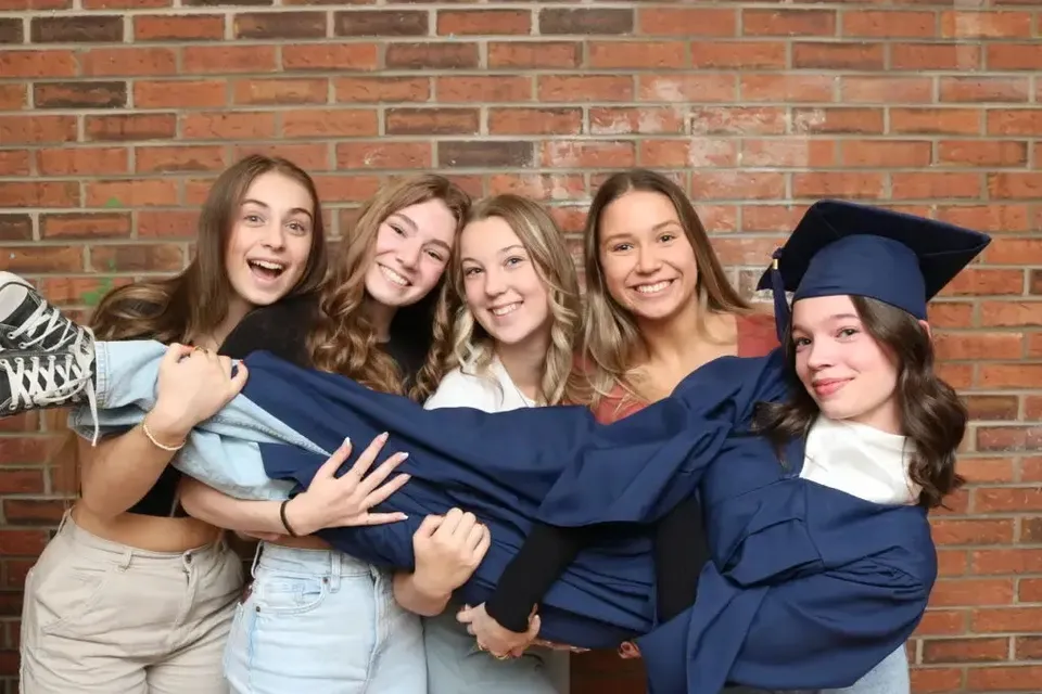 Un gruppo di giovani donne con l'abito da diploma posa davanti a un muro di mattoni nel campus della École secondaire publique L'Académie de la Seigneurie.