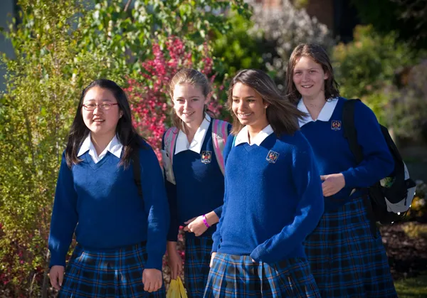 Cuatro estudiantes con uniformes escolares están juntas en un jardín en el campus de Garin College.