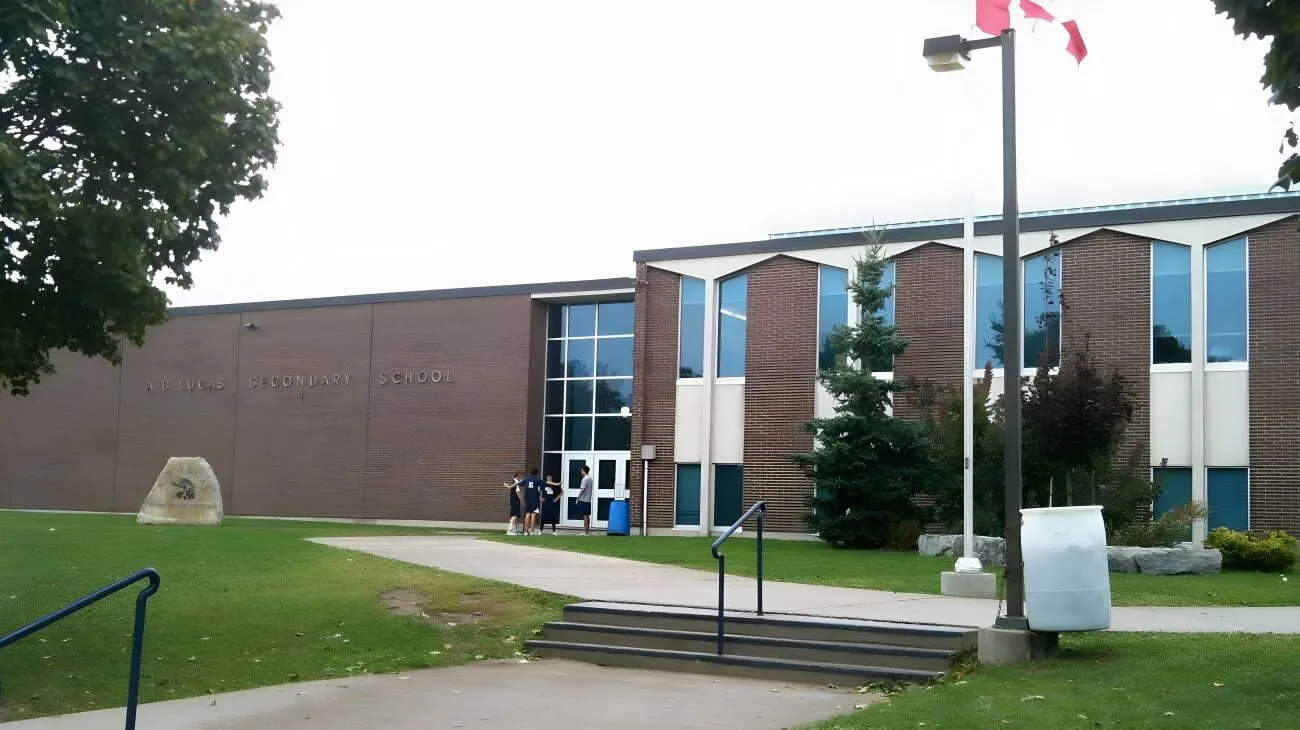 El moderno edificio de ladrillo de la A.B. Lucas Secondary School con grandes ventanas y la bandera canadiense en el campus.