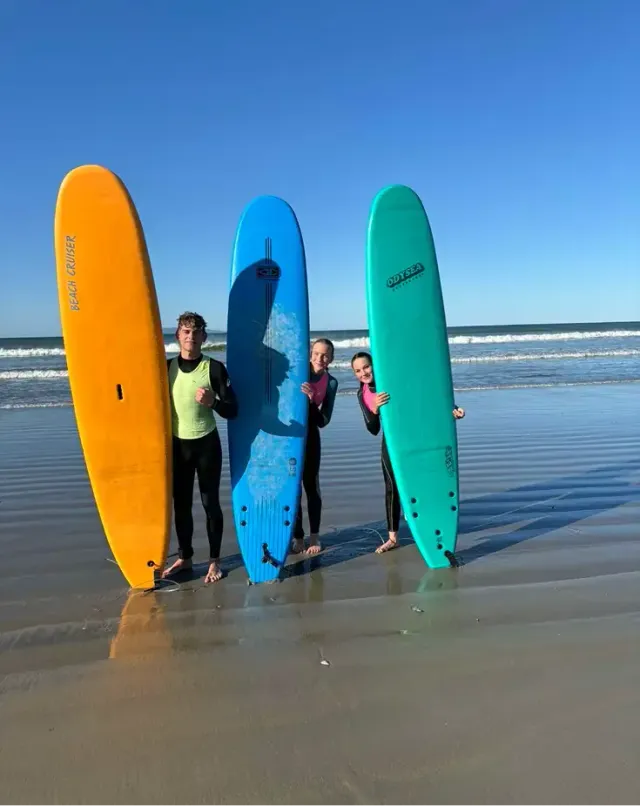 Tre ragazzi in muta posano con le tavole da surf sulla spiaggia