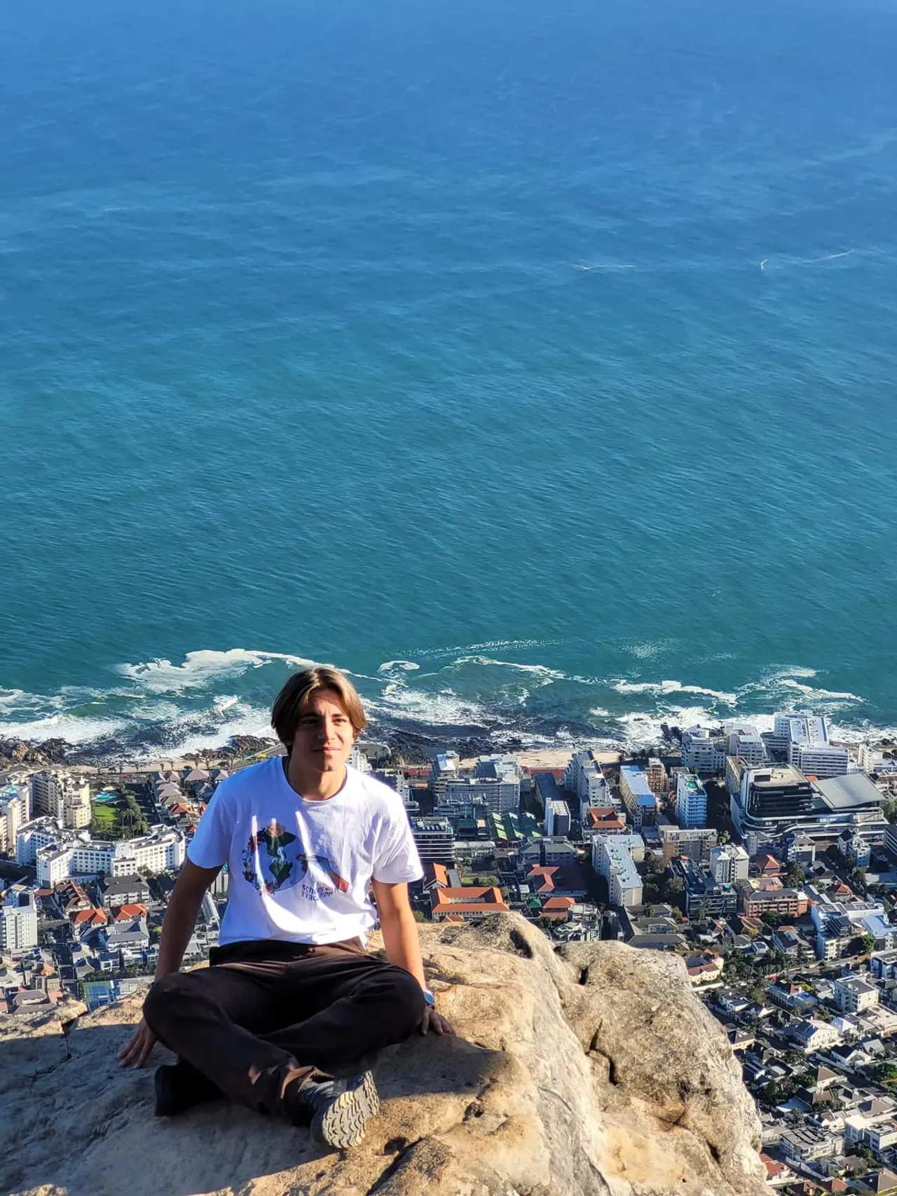 Studente seduto a gambe incrociate su una roccia sopra l'oceano e Città del Capo