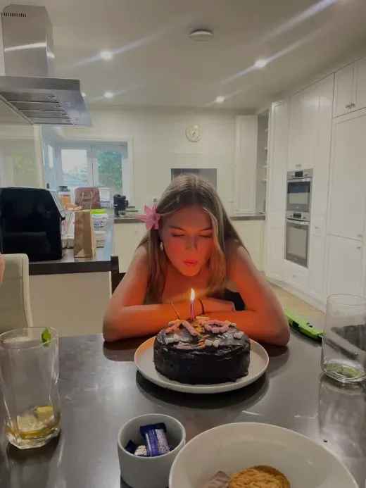 Chica soplando la vela de una tarta de chocolate en la cocina de la casa