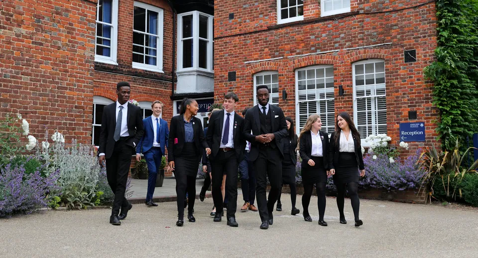 Un gruppo di persone cammina insieme davanti a un edificio in mattoni nel campus della Ashford School.