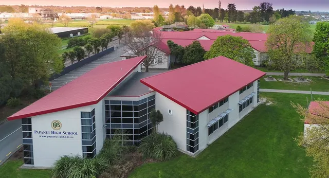 L'edificio a più piani con il tetto rosso della Papanui High School si trova circondato da alberi in un ambiente rurale.