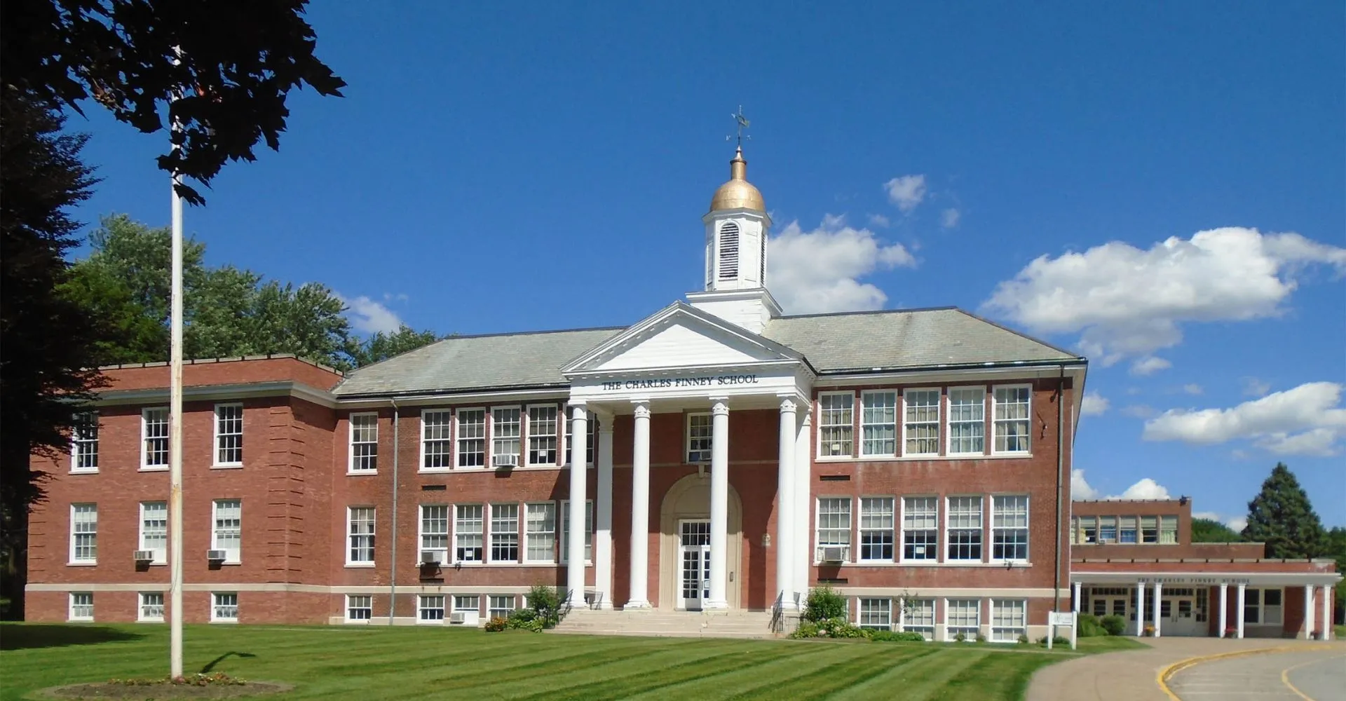 L'edificio storico in mattoni con una torre campanaria bianca si trova nel campus della The Charles Finney School sotto un cielo blu.