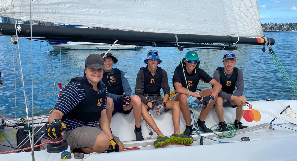 Studenti della Whangarei Boys’ High School seduti in tenuta uniforme su una barca a vela in mare aperto.