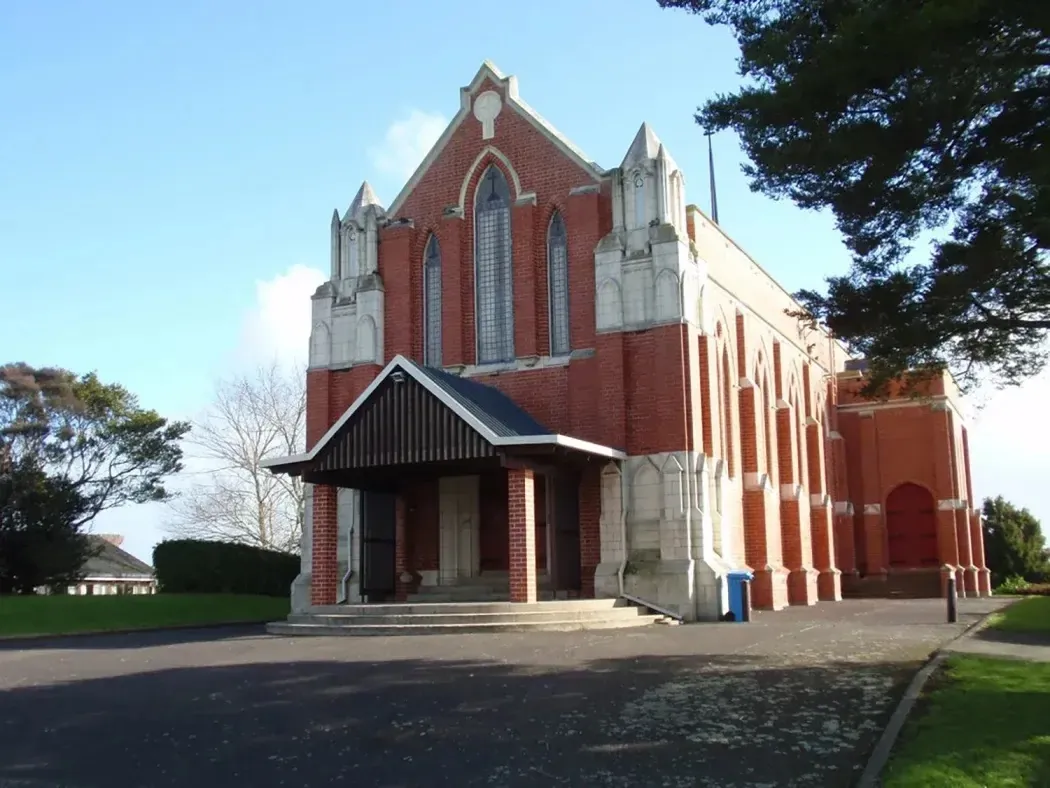 Una gran iglesia de ladrillo rojo de estilo gótico se encuentra ante árboles verdes en el recinto de Wesley College.