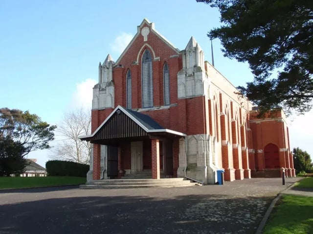 Una grande chiesa in mattoni rossi in stile gotico si erge davanti ad alberi verdi nel campus del Wesley College.