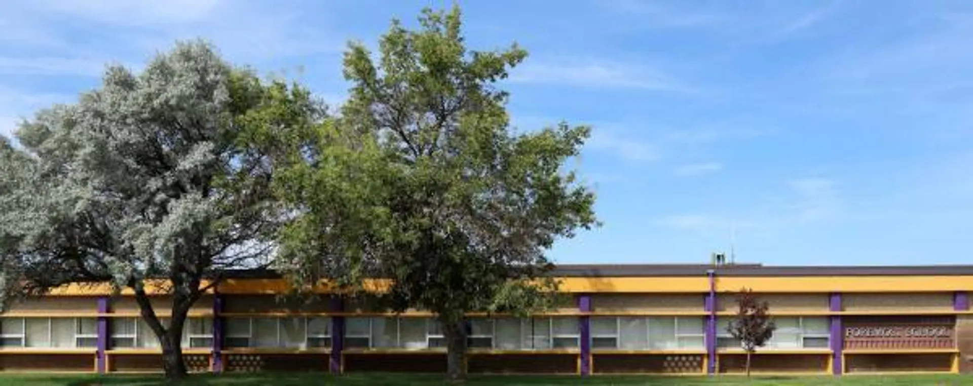 L'edificio scolastico moderno della Foremost School è incorniciato da una chioma verde ed è visibile contro un cielo blu.