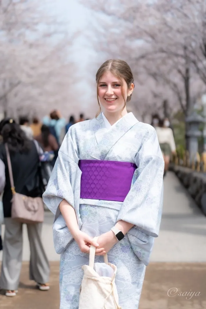 Ragazza sorridente in kimono chiaro con obi viola su un viale di ciliegi in fiore in Giappone