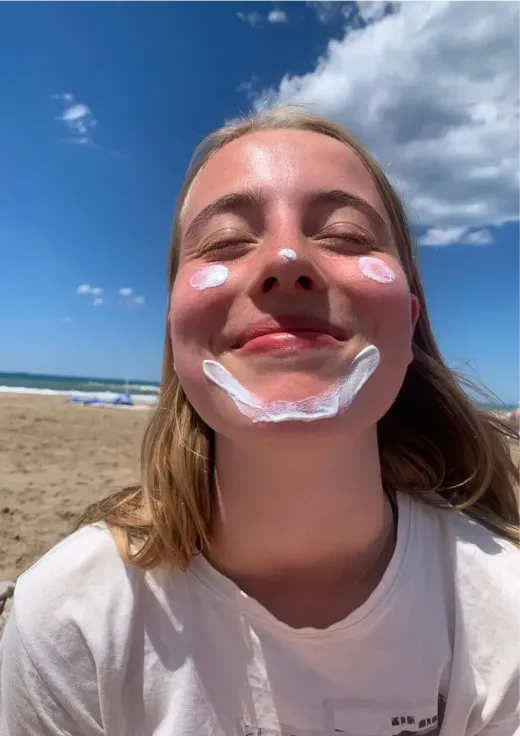 Mädchen mit einem aufgemalten Lächeln aus Sonnencreme im Gesicht an einem Strand in Spanien