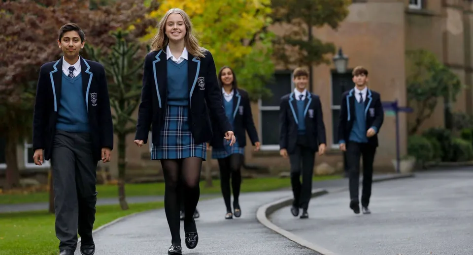 Un gruppo di studenti in uniforme scolastica cammina lungo un viale circondato da aree verdi nel campus del Tettenhall College.
