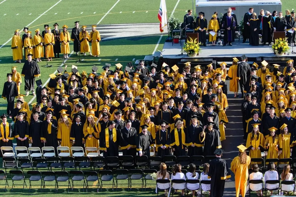 Un grande gruppo di diplomati in toga gialla e nera si trova sul palco dell'Oak Park Unified School District.