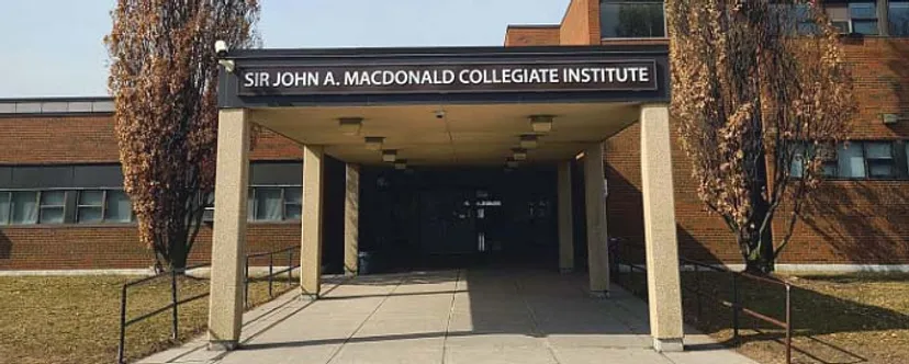 Si vede l'ingresso del Sir John A. Macdonald Collegiate Institute con un vialetto coperto e un edificio in mattoni.