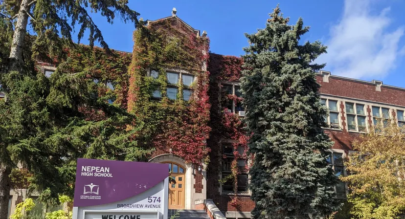 Si vede l'edificio in mattoni della Nepean High School con pareti coperte di edera e circondato da conifere.