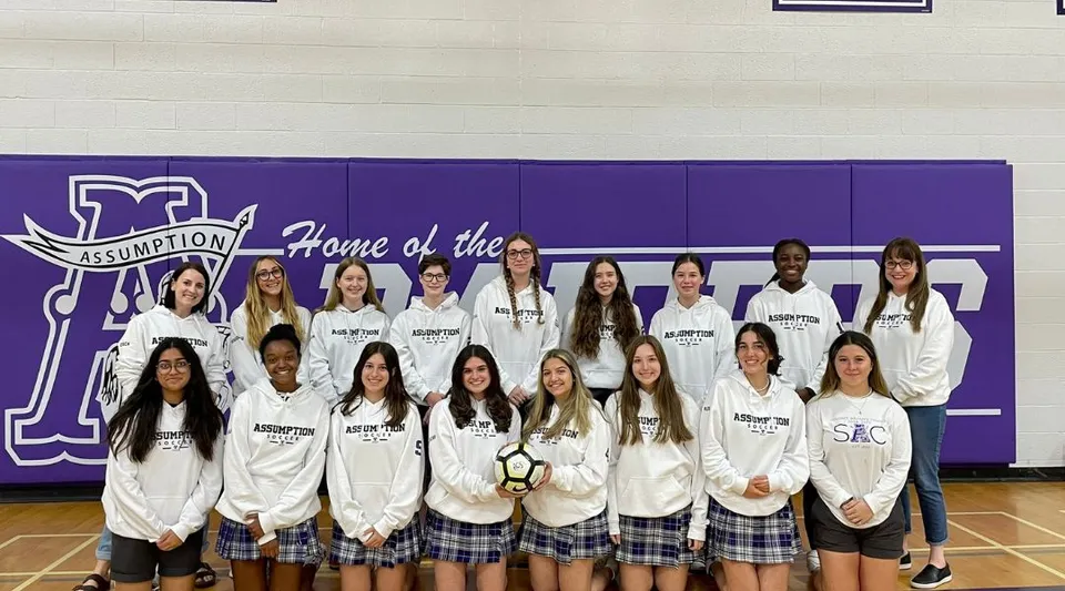 Un gruppo di studentesse in divisa bianca davanti a uno striscione viola nel campus della Assumption College Catholic High School.