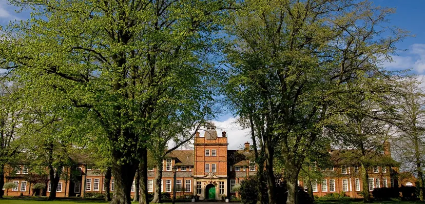 Edificio storico in mattoni della Dauntsey’s School circondato da alberi verdi sotto un cielo blu.