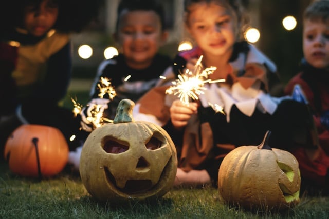 Kinder in Halloween-Kostümen mit Wunderkerzen hinter geschnitzten Kürbissen