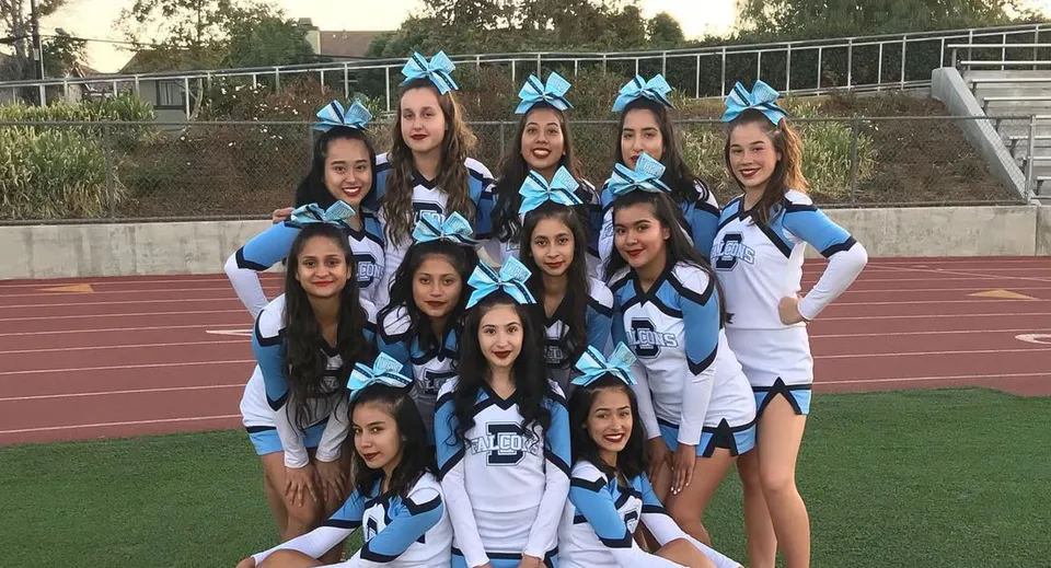 Un gruppo di ragazze in divisa da cheerleading posa insieme sul campo sportivo del Duarte Unified School District.
