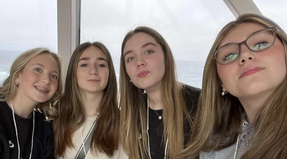 Quattro studentesse della Holy Trinity High School posano davanti a una finestra con vista sul cielo nuvoloso.