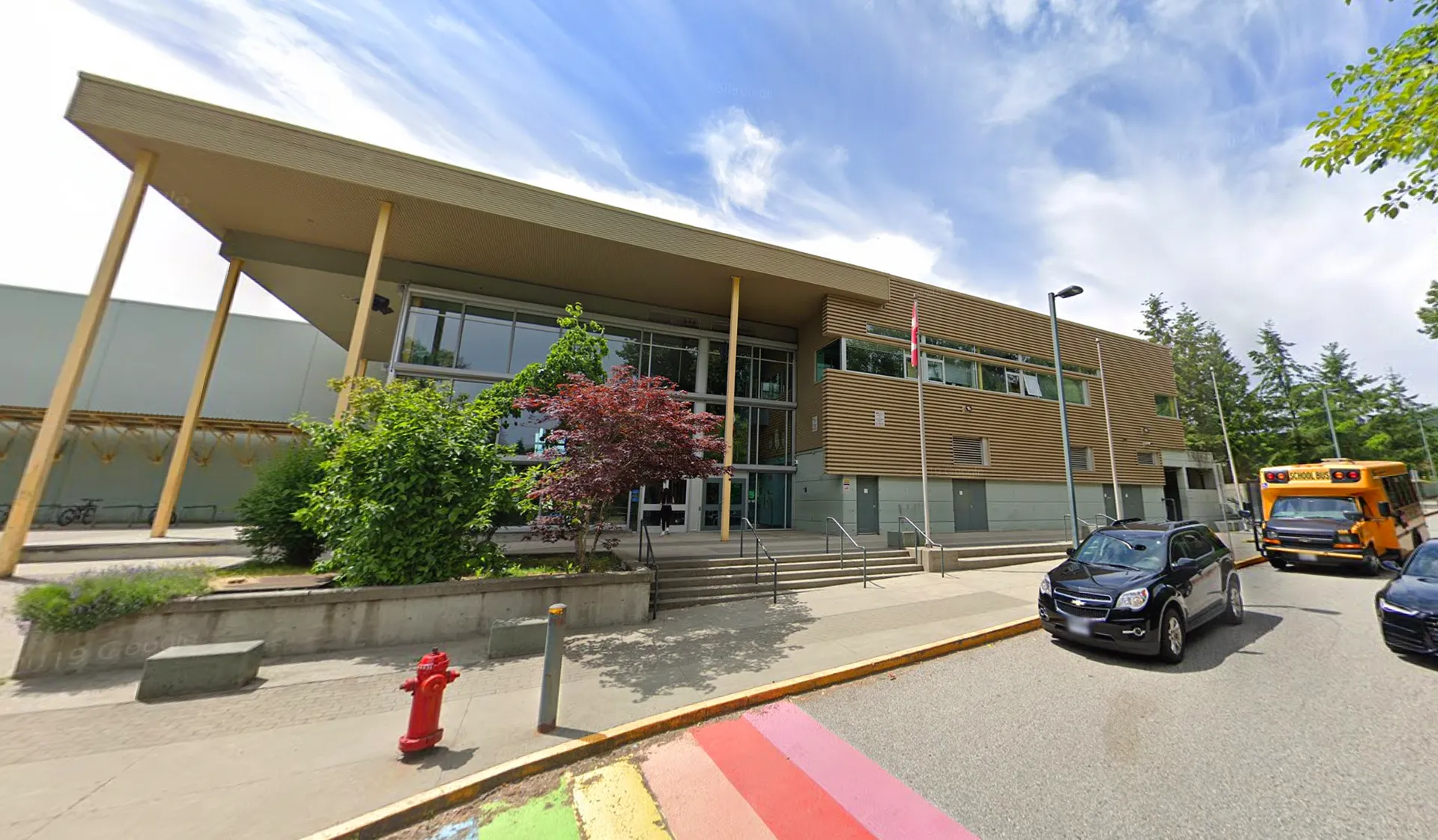 L'edificio moderno a più piani della Burnaby Mountain School con facciata in vetro e ingresso coperto è circondato da alberi.
