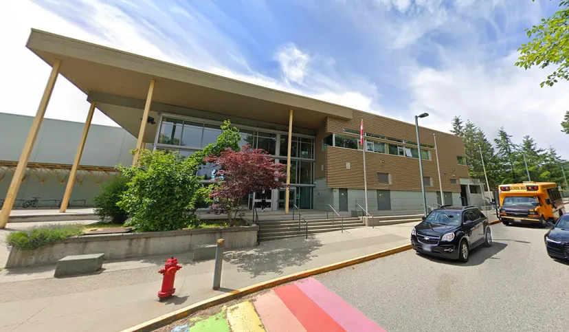 L'edificio moderno a più piani della Burnaby Mountain School con facciata in vetro e ingresso coperto è circondato da alberi.