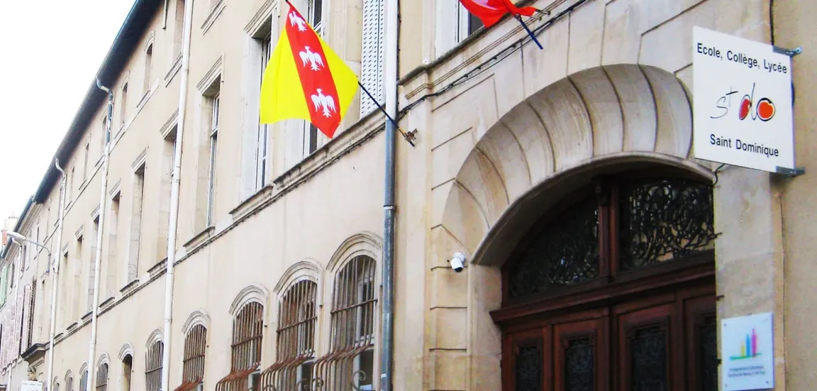 Historisches Schulgebäude mit Steinfassade, Rundbogenportal und Flaggen, Schild Ecole Collège Lycée Saint Dominique am Eingang