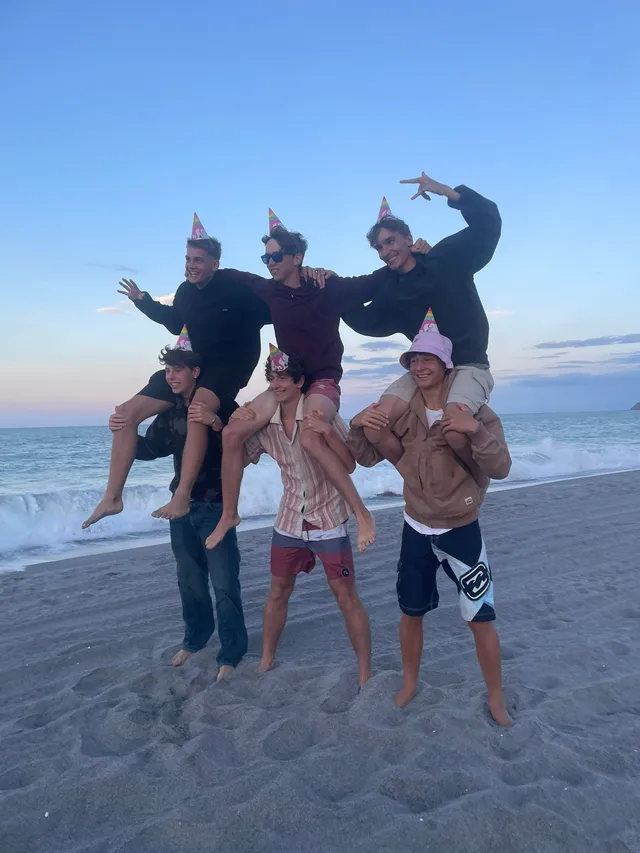 Seis chicos con gorros de fiesta haciendo el tonto en la playa al anochecer
