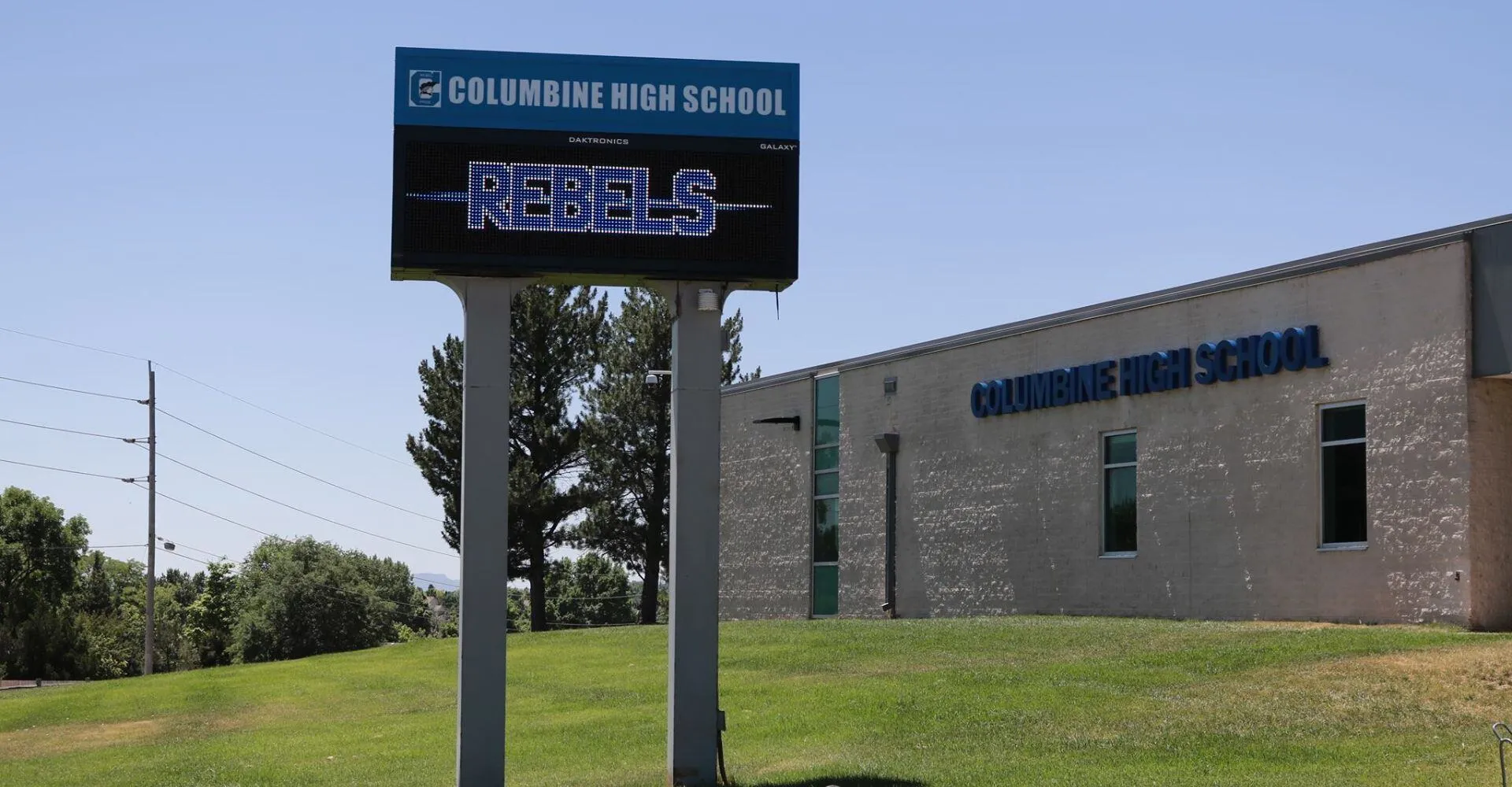 Il grande cartello della Columbine High School con la scritta e la mascotte Rebels sullo sfondo del cielo blu e degli alberi nel campus delle Jeffco Public Schools.