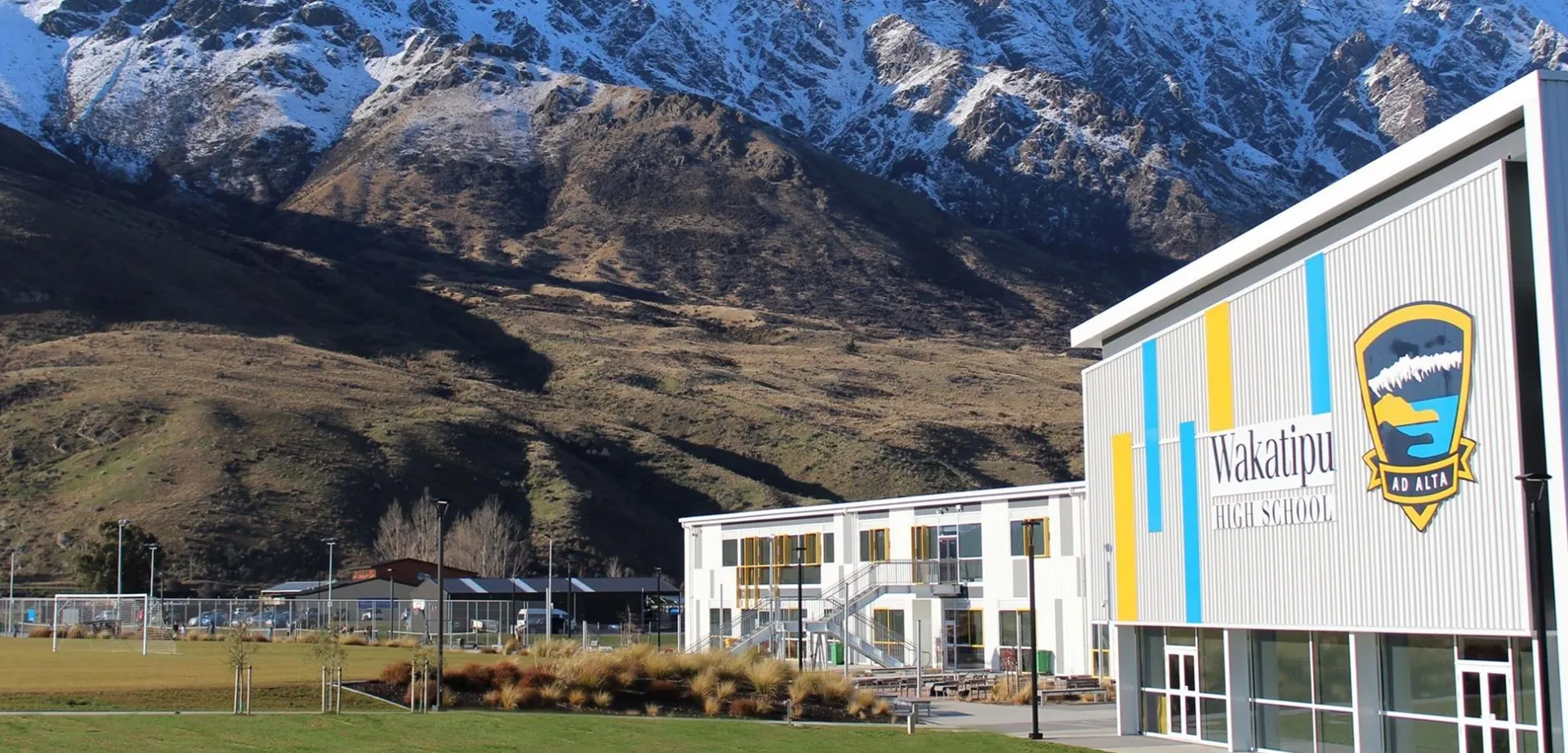 L'edificio colorato della Wakatipu High School si trova davanti a montagne innevate e a un paesaggio verde.