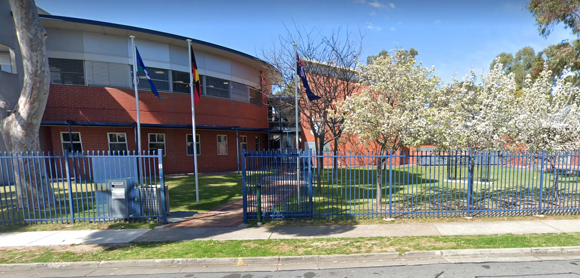 L'edificio principale moderno a più piani della Woodville High School con tetto a volta si trova davanti a un'area verde recintata e alberi in fiore.